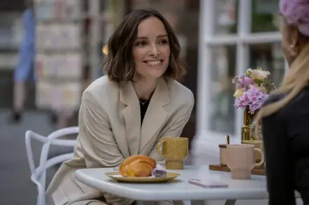 A scene from the TV show Ted Lasso featuring Jodi Balfour, smiling at a table with coffee and pastries, surrounded by flowers in an inviting café setting. 8K Ultra HD wallpaper.