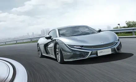 HD desktop wallpaper featuring a sleek Mullen Qiantu K50 electric car driving on a curved highway with a city skyline in the background.