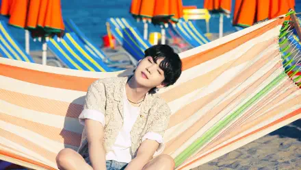 4K Ultra HD desktop wallpaper featuring BTS member Suga (Min Yoongi) relaxing on a striped hammock at a vibrant beach setting with colorful umbrellas in the background.