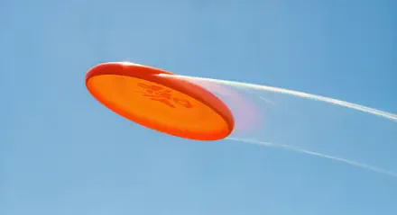 A vibrant orange frisbee soaring through a clear blue sky, captured in sharp detail as part of an outdoor flying disc game.