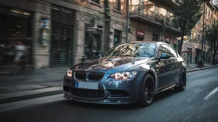 Blue BMW M3 driving through a tree-lined urban street with motion blur, HD PC desktop wallpaper and background showcasing glossy reflections and a sporty stance.