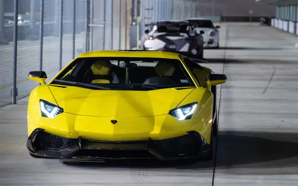 Front view of a yellow Lamborghini in a lit tunnel, high-detail 5K Ultra HD PC desktop wallpaper showing headlights on and a second car trailing behind.