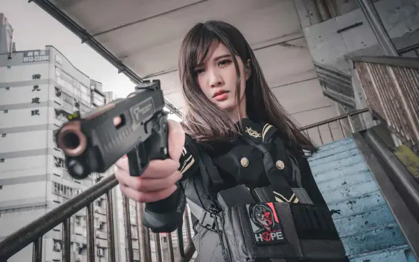 4K Ultra HD PC desktop wallpaper: woman in tactical gear aims a handgun at the viewer on an urban stairwell, gritty city buildings in the background.