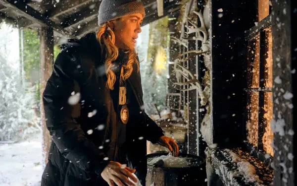Melissa Roxburgh in a snowy scene from the TV show The Hunting Party (2025), wearing a beanie and coat, engaging with a cozy fireplace backdrop. HD wallpaper for desktop backgrounds.