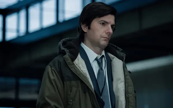 A 4K Ultra HD image from the TV show *Severance*, featuring Adam Scott in a contemplative moment, dressed in a coat and tie, set in a modern, industrial environment.