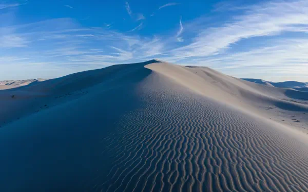 A stunning 4K Ultra HD image of sweeping sand dunes under a bright blue sky, showcasing intricate patterns on the sand and gentle ridges that lead to the horizon.