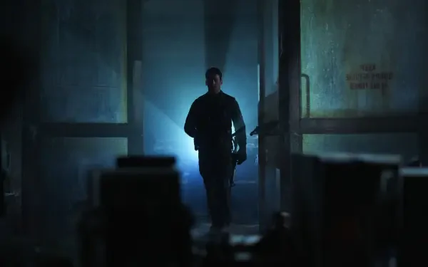 A dramatic scene from the movie The Gorge (2025) featuring Miles Teller. The image shows a lone figure walking through a dimly lit corridor, enhanced by striking light effects.