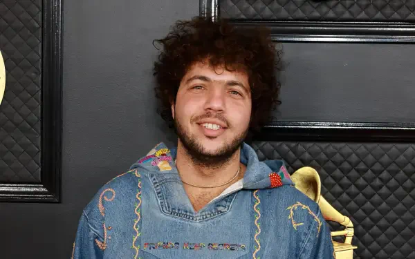 Benny Blanco smiles in a colorful hoodie against a sleek black backdrop, creating a vibrant HD desktop wallpaper for music enthusiasts.