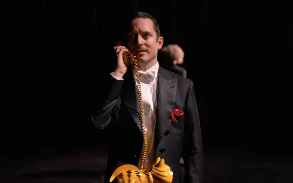 A scene from the TV show Yellowjackets, featuring Elijah Wood in a tuxedo, holding a whimsical phone. The image is a striking 4K Ultra HD wallpaper.