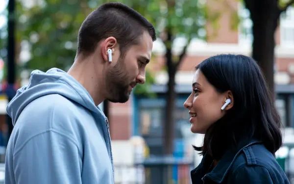 A 4K Ultra HD wallpaper featuring a man and woman smiling at each other, both wearing white earbuds, set against a blurred urban background with greenery.