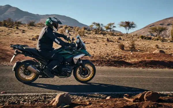 A BMW R1300GS motorcycle is riding along a desert road, with mountains in the background, captured in stunning 4K Ultra HD detail.