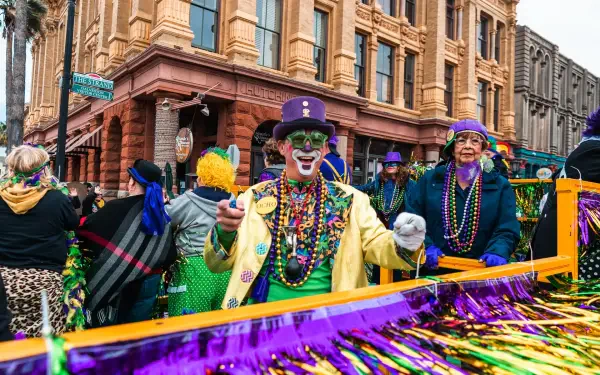 A vibrant Mardi Gras festival scene featuring costumed participants adorned in beads and masks, set against festive decorations and historic architecture. HD wallpaper showcasing celebration.