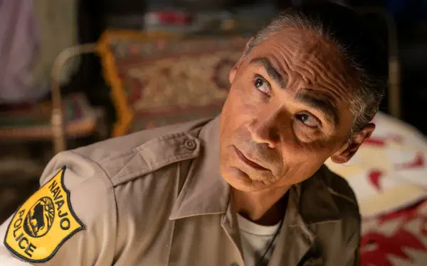 A captivating HD wallpaper from the TV show Dark Winds, featuring Zahn McClarnon in his character's uniform, gazing thoughtfully as he investigates a scene.