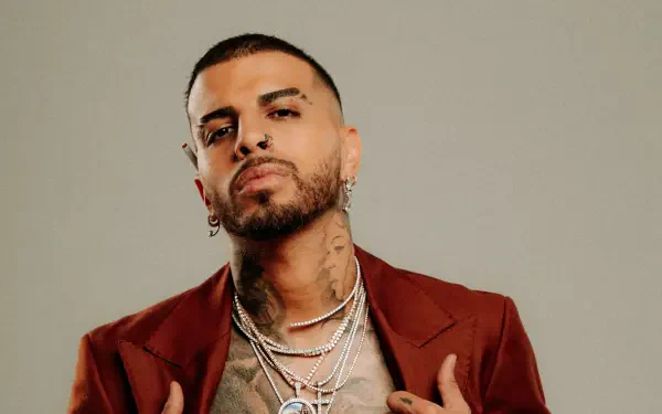 HD PC desktop wallpaper featuring Rauw Alejandro, showcasing him in a confident pose with layered necklaces, earrings, and a maroon jacket, representing music and style.
