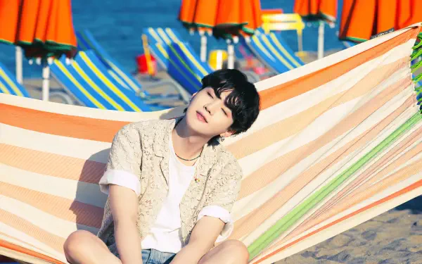 4K Ultra HD desktop wallpaper featuring BTS member Suga (Min Yoongi) relaxing on a striped hammock at a vibrant beach setting with colorful umbrellas in the background.