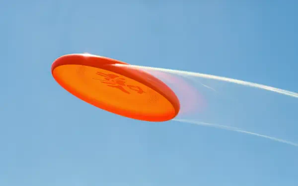 A vibrant orange frisbee soaring through a clear blue sky, captured in sharp detail as part of an outdoor flying disc game.