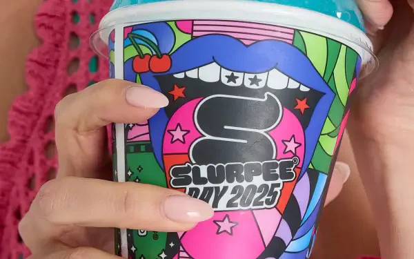 Close-up of hands holding a colorful Slurpee cup with bold graphic design, featuring nails and vibrant artwork, set as a HD man-made PC desktop wallpaper background.