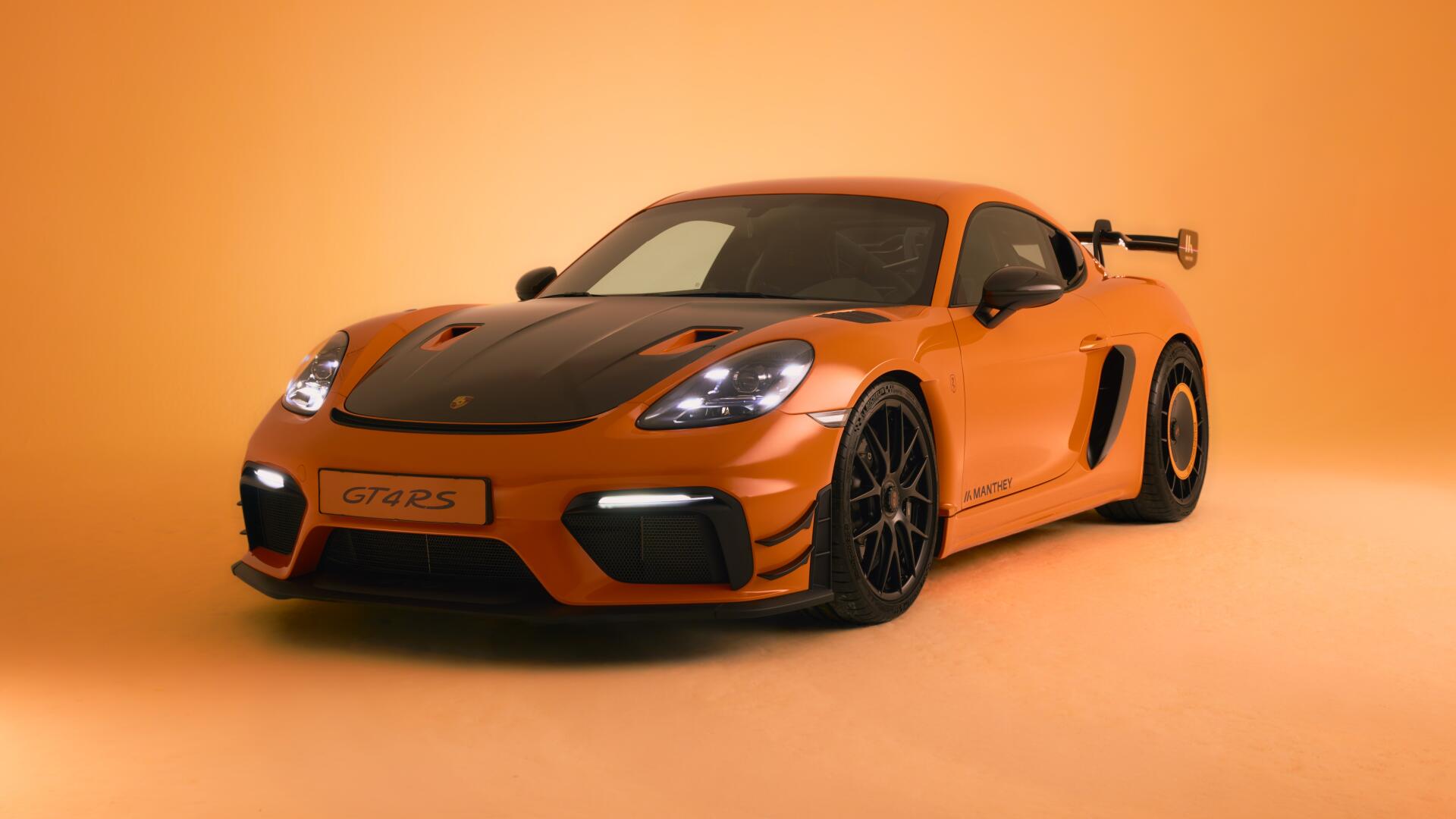 Orange Porsche 718 Cayman GT4 sports car, front three-quarter view in a studio with matching orange backdrop — 4K Ultra HD PC desktop wallpaper