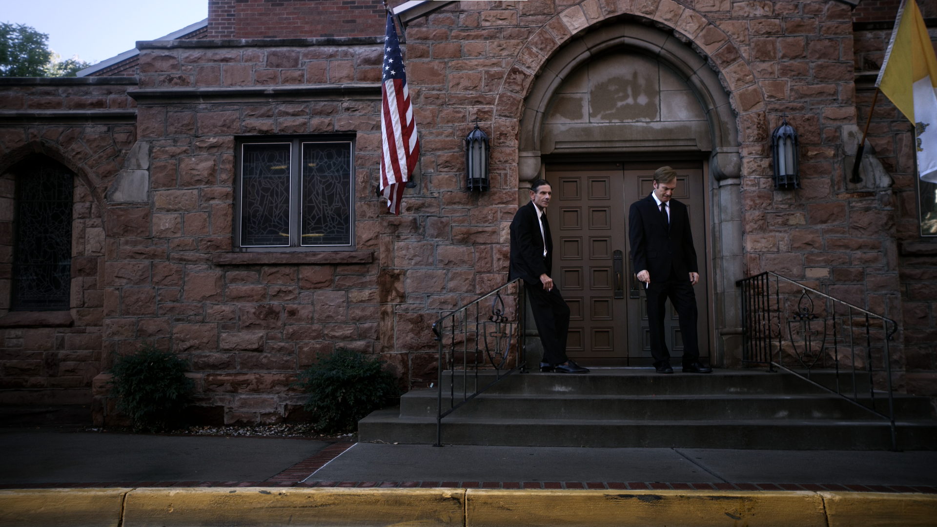 HD PC desktop wallpaper and background of TV show Better Call Saul featuring two suited men on stone church steps beneath an American flag.