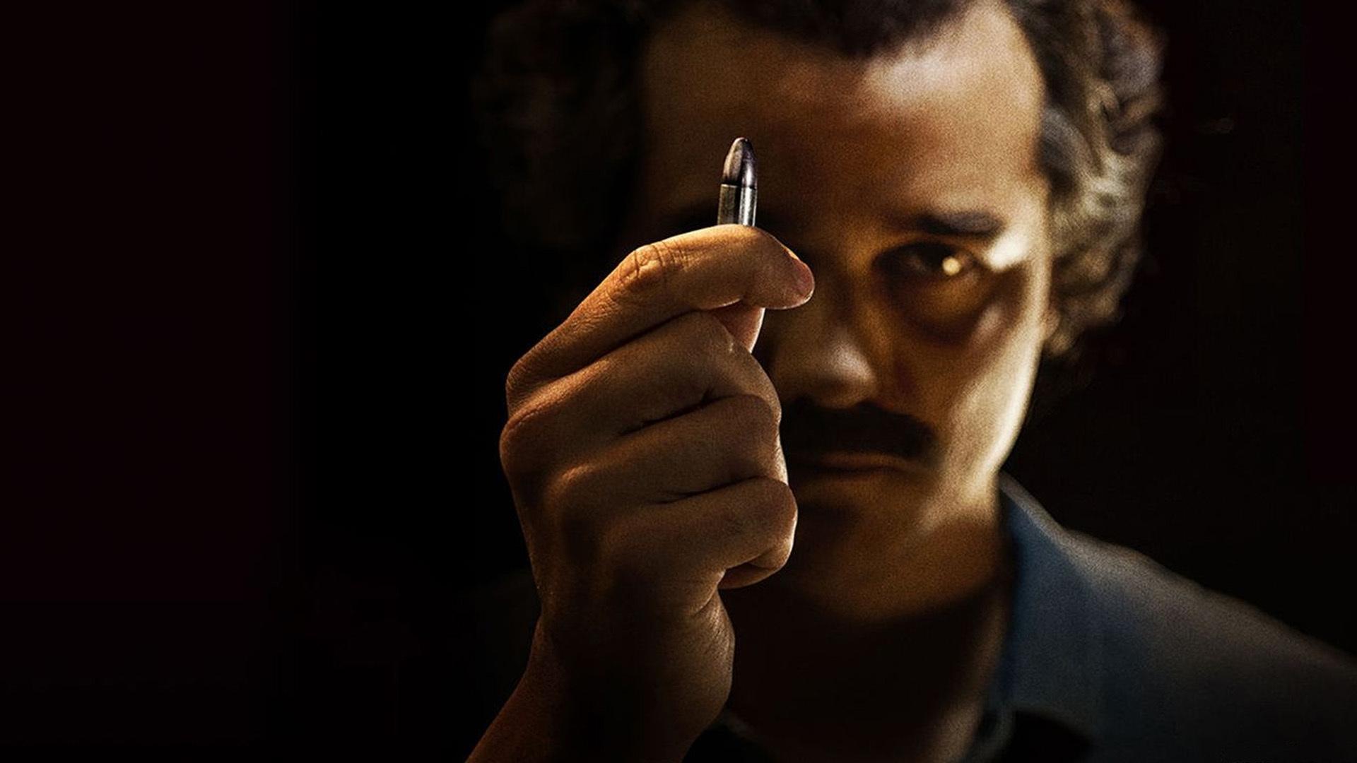 Narcos HD PC desktop wallpaper and background: shadowed man holds a single bullet between thumb and forefinger, intense gaze in a moody low-light portrait.