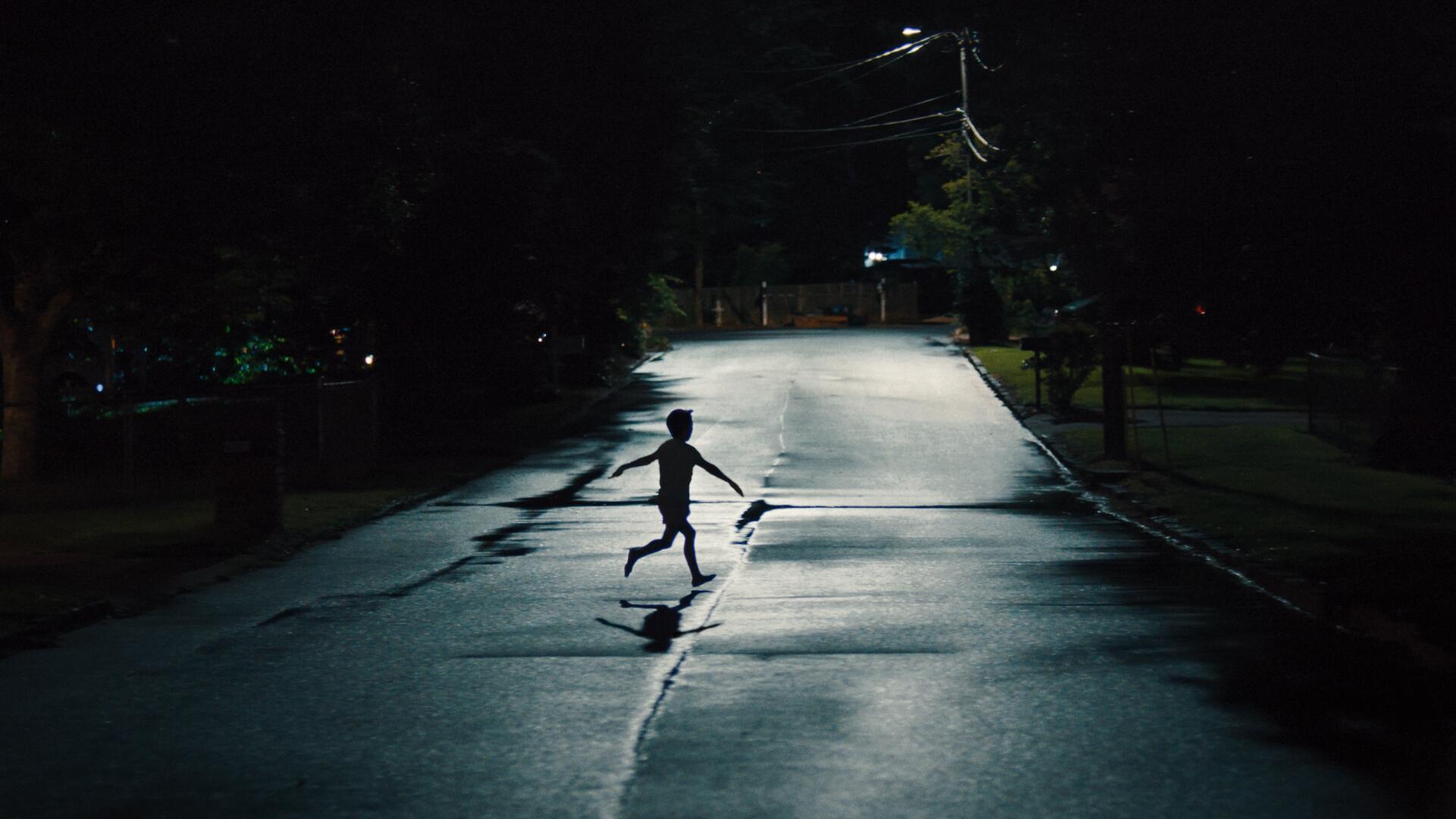 4K Ultra HD PC desktop wallpaper: lone silhouetted figure runs across a wet, dimly lit street at night, clutching a long object that looks like a weapon, casting a stretched shadow.