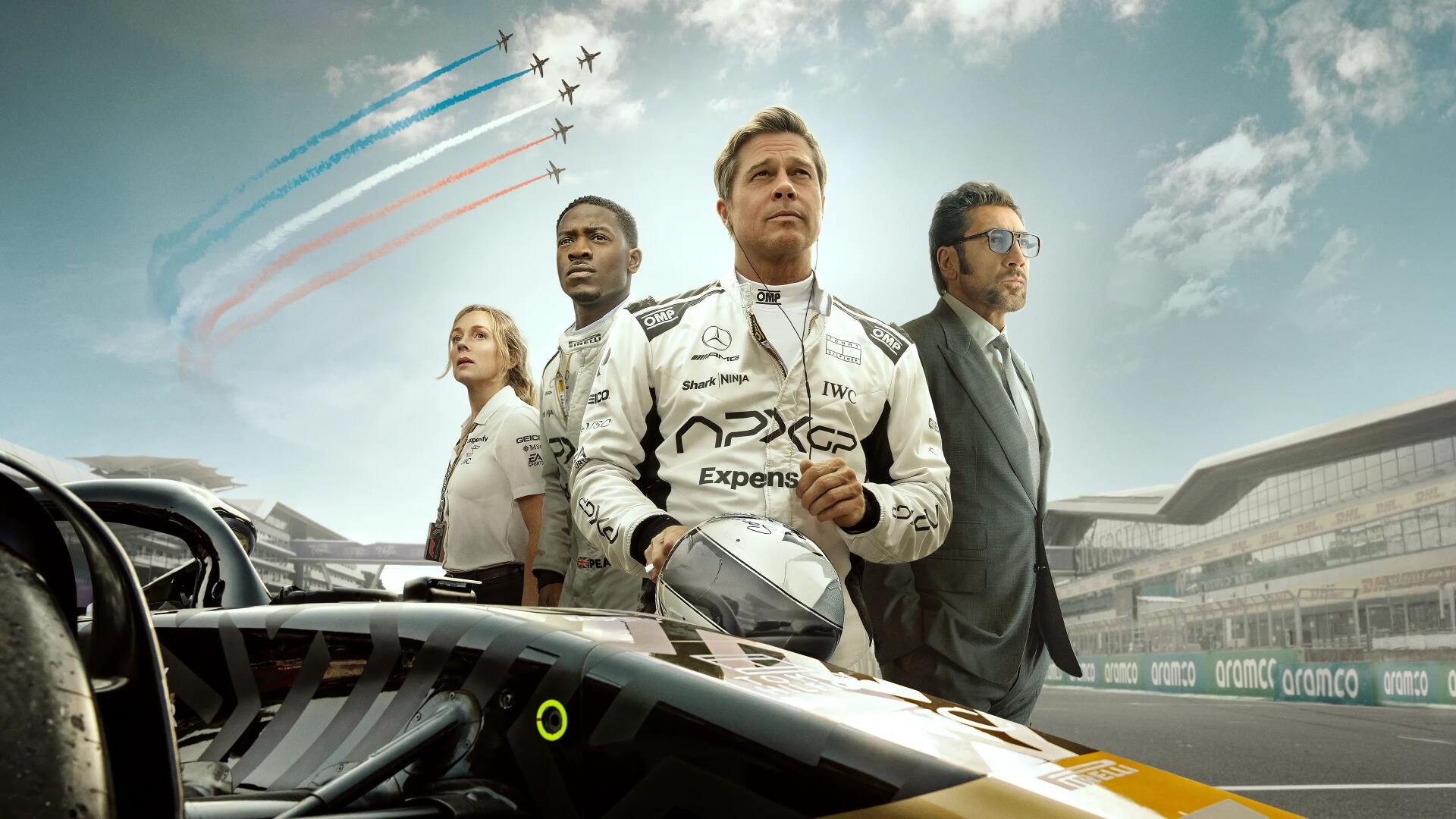 F1 (2025) 4K Ultra HD PC desktop wallpaper: an F1 driver in suit holds his helmet beside teammates and a race car on the grid, jets streak the cloudy sky.