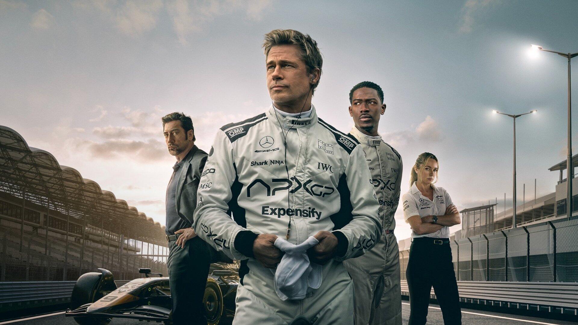 F1 (2025) HD PC desktop wallpaper — three racing team members in white suits stand on the pit lane beside an F1 car at dusk, with stadium lights and grandstands in the background.