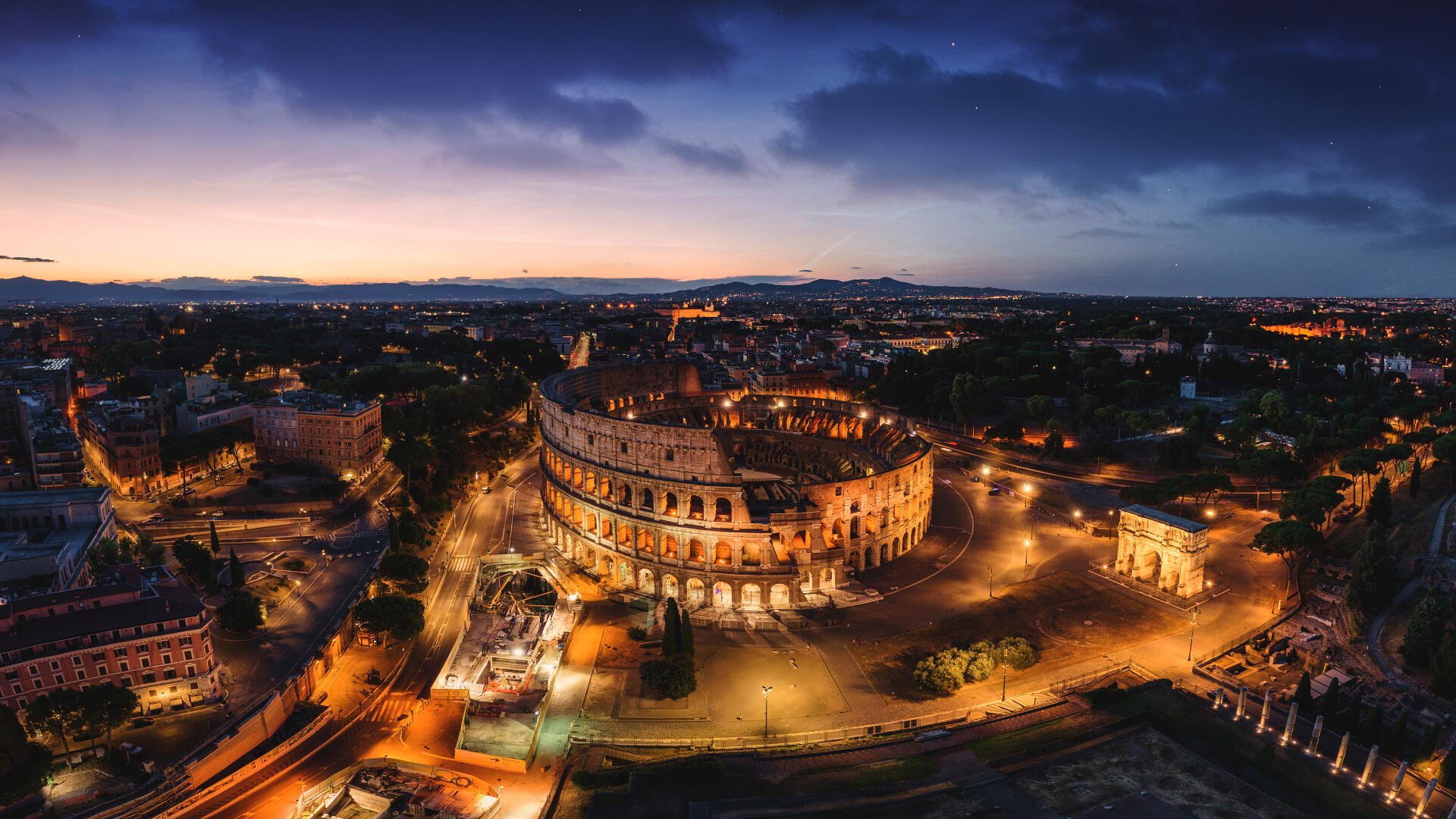 4K Ultra HD desktop wallpaper: aerial night cityscape of Rome, Italy, featuring the illuminated Colosseum and surrounding streets.