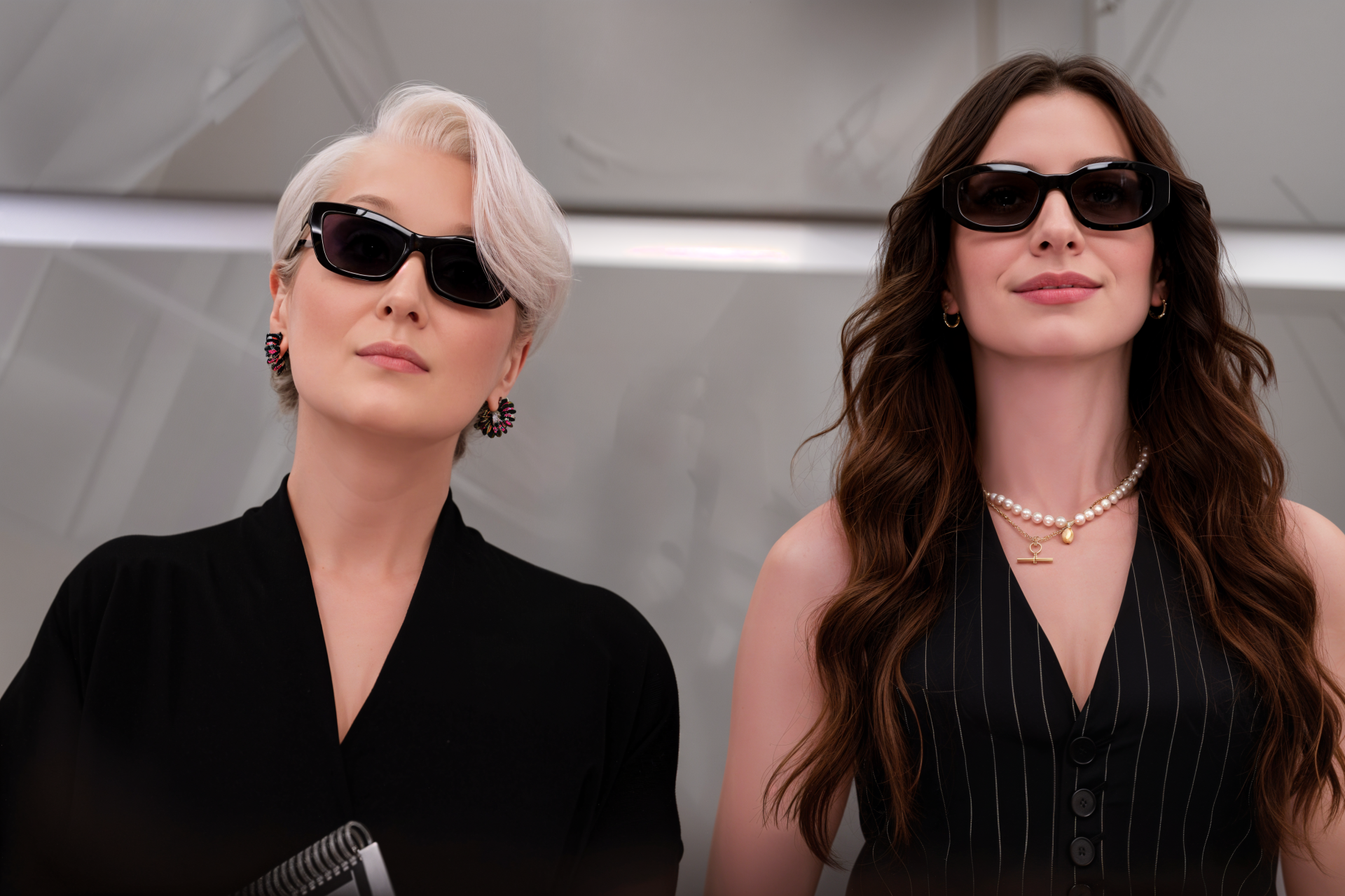 4K Ultra HD desktop wallpaper for The Devil Wears Prada 2: two stylish women in sunglasses and tailored black outfits, striking confident poses against a minimalist, neutral backdrop.