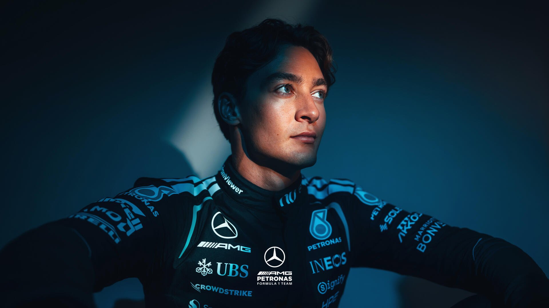 Moody portrait of a Mercedes AMG F1 driver in team race suit, gazing into light — 2K Quad HD PC desktop wallpaper/background with F1 racing theme.