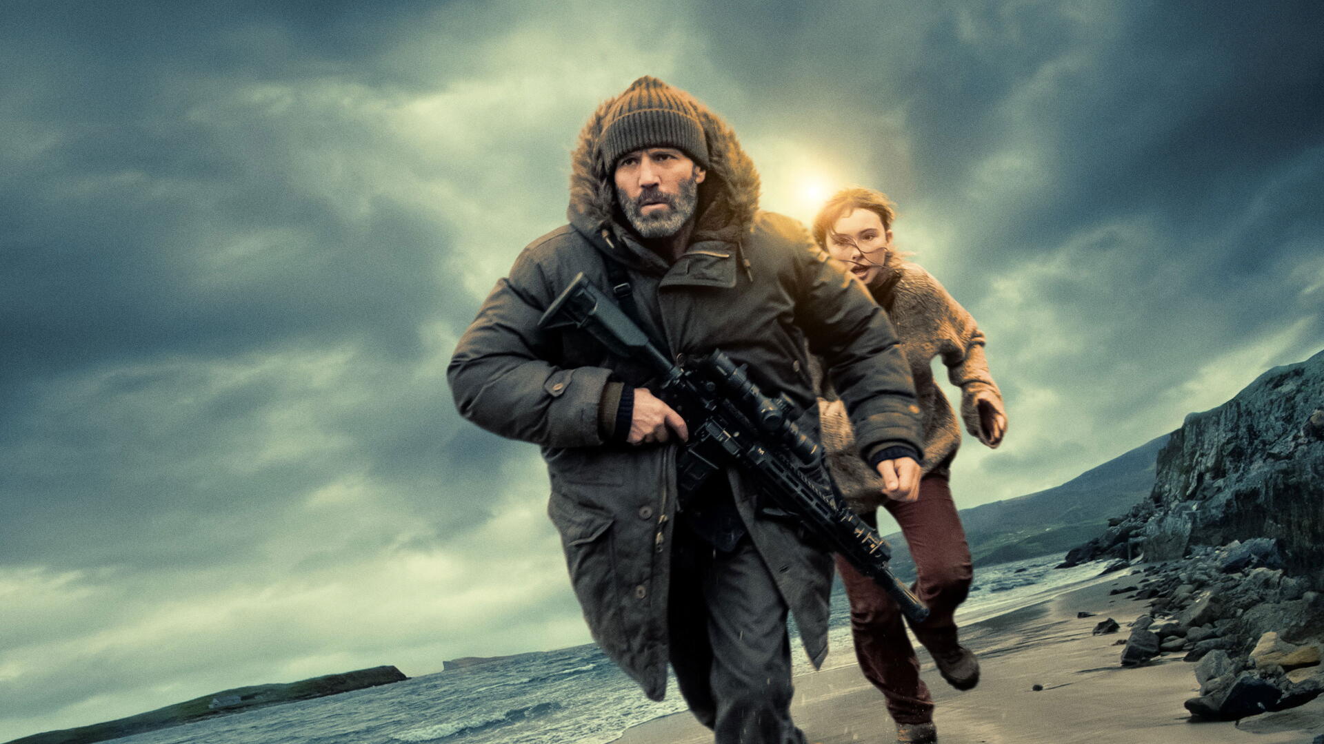 4K Ultra HD PC desktop wallpaper: two bundled figures race along a stormy shore, man with rifle leading a woman as they head toward shelter under dark, turbulent skies.