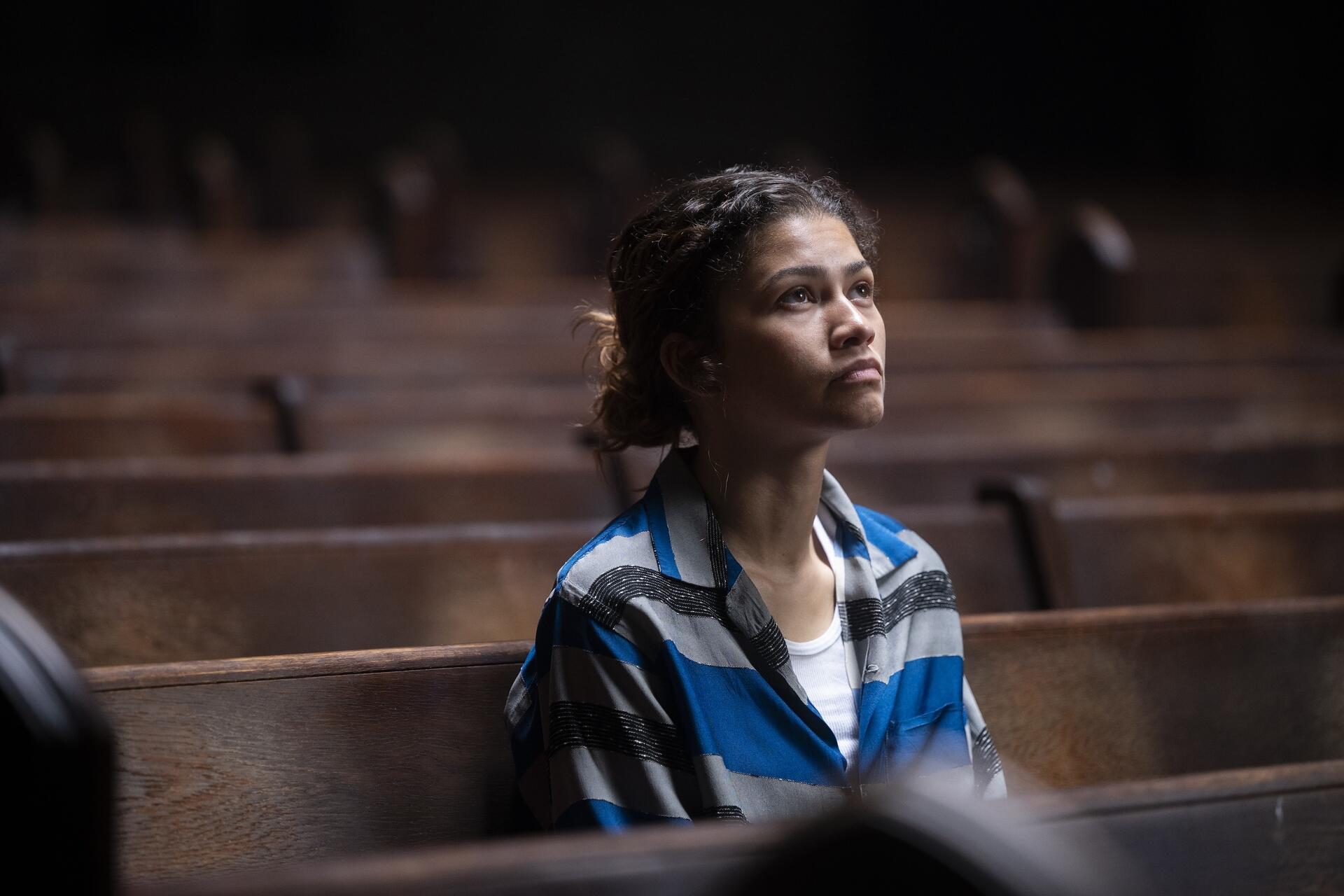 HD PC desktop wallpaper of a contemplative young actress from a TV drama, seated alone on wooden pews in dim light, gazing upward with a solemn expression.