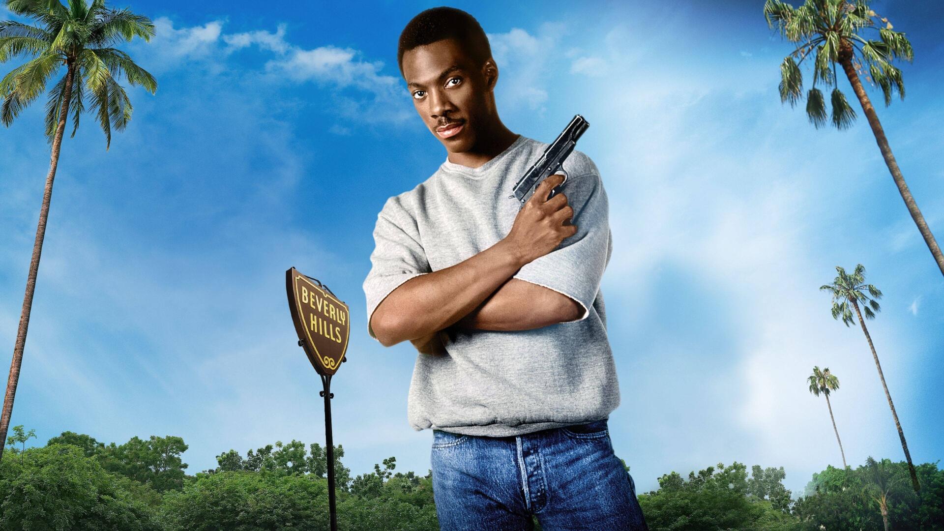 4K Ultra HD PC Desktop Wallpaper and Background: a man in jeans and a gray sweatshirt holds a pistol with arms crossed beneath a bright blue sky, palm trees and a roadside sign.