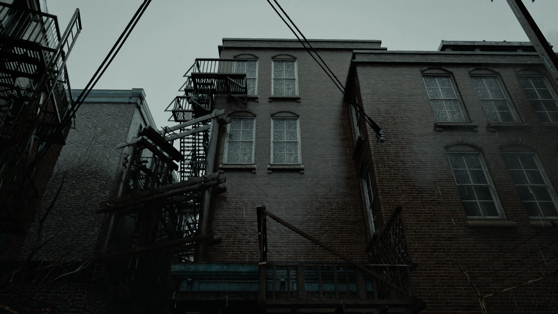 Resident Evil Requiem 2K Quad HD PC desktop wallpaper: moody desaturated alley of brick buildings with fire escapes, overhead wires and a gloomy sky.