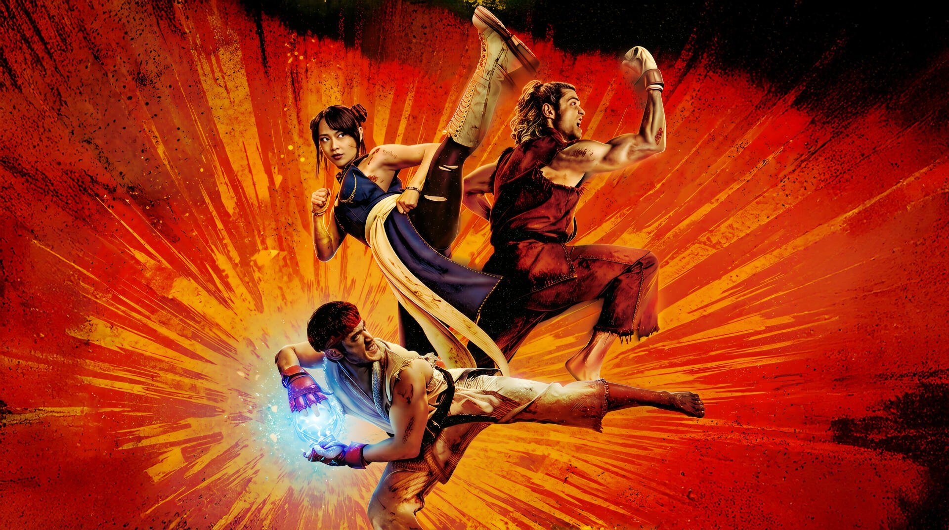 Street Fighter (2026) 2K Quad HD PC wallpaper and background: three fighters mid-air — high kick, spinning kick, energy-charged punch — over an explosive orange burst.