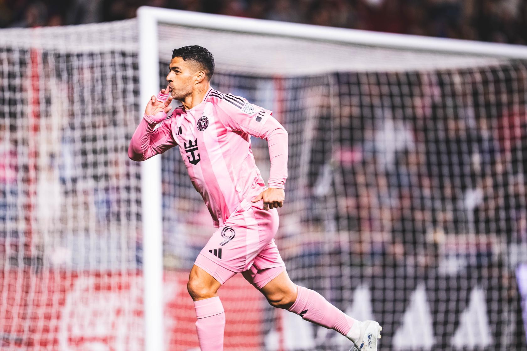 HD desktop wallpaper of an Inter Miami CF soccer forward in pink kit celebrating a goal by the net, sprinting with a finger to his lips amid a packed stadium.