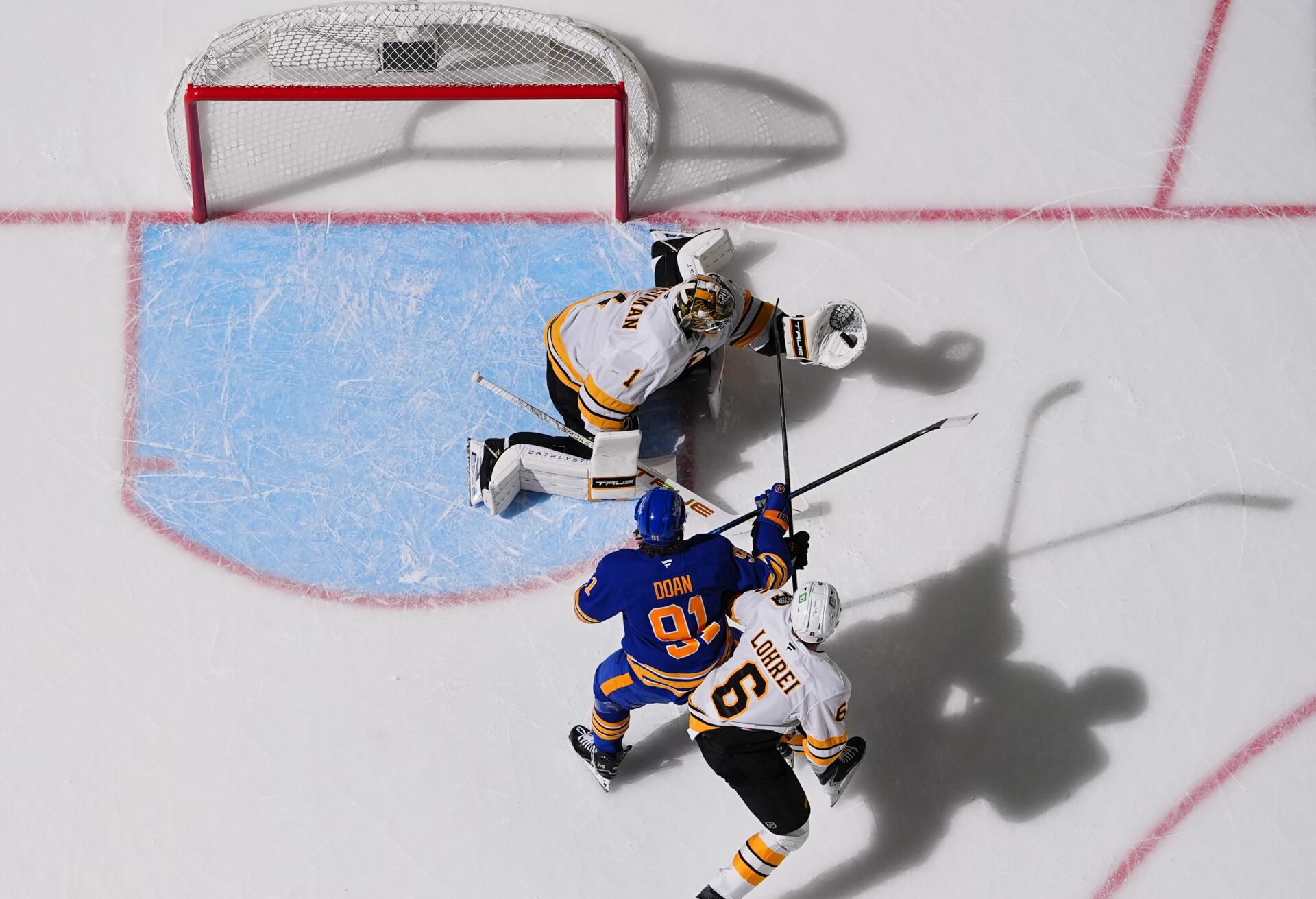 Overhead hockey photography: NHL action between Buffalo Sabres and Boston Bruins at the crease — goalie and two skaters with long shadows on the ice. 2K Quad HD PC desktop wallpaper background.
