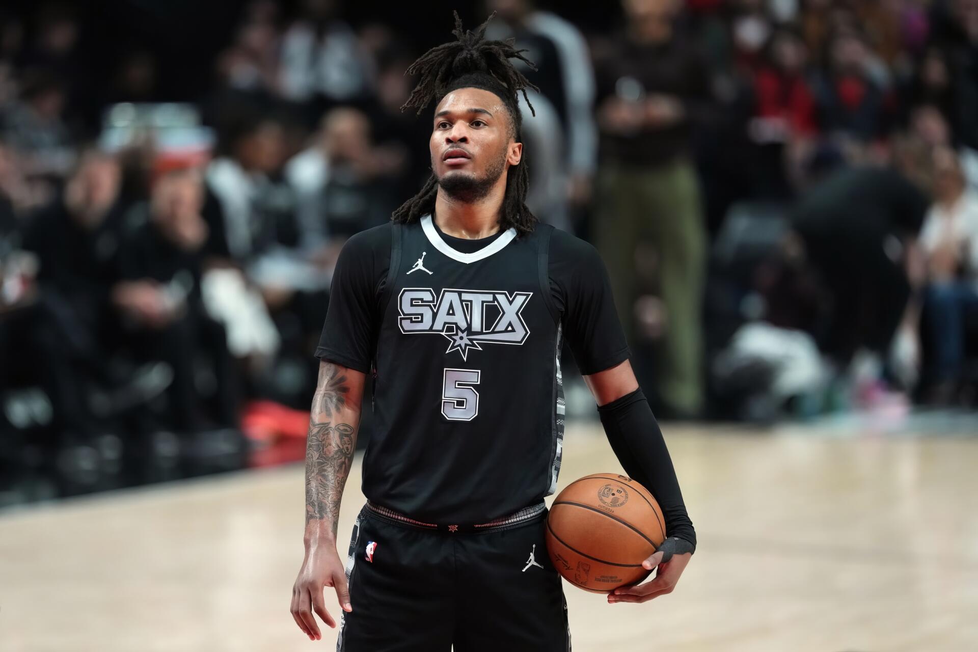 2K Quad HD PC desktop wallpaper of an NBA player in a San Antonio Spurs jersey holding a basketball on the court with arena crowd in the background.