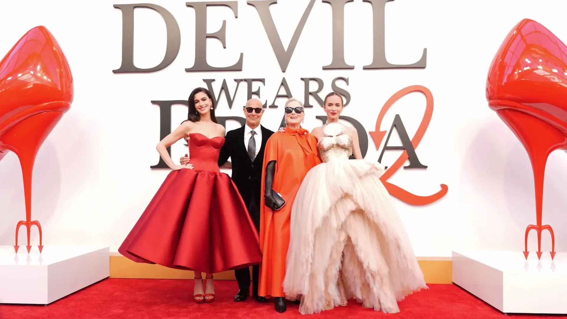 2K Quad HD desktop wallpaper: red-carpet portrait of The Devil Wears Prada 2 principal cast in elegant gowns and suits before a large logo and oversized red-heel props.