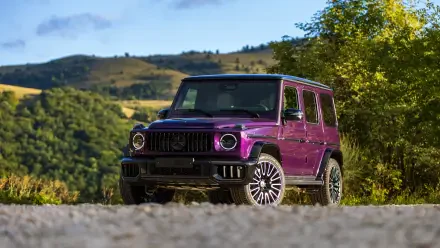 Purple Mercedes-AMG G63 SUV on a gravel road with green hills in the background — 5K Ultra HD PC desktop wallpaper and background.