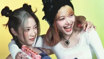 Two smiling South Korean K-pop idols in playful outfits and accessories, laughing close-up against a soft yellow backdrop — 4K PC desktop wallpaper.
