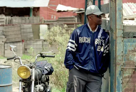 4K Ultra HD PC wallpaper: gritty Man on Fire (2004)–style gangster scene — a man in a navy jacket and cap leans by a doorway next to a motorcycle in a sunlit, rundown lot.