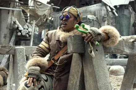 Live-action TV show image of Usopp from One Piece in a fur-lined outfit with goggles and slingshot, gritty dockside setting — 2K Quad HD PC desktop wallpaper/background.