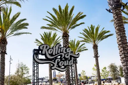 HD PC desktop wallpaper background: outdoor music festival scene with palm trees framing a Rolling Loud entrance sign beneath a clear blue sky.