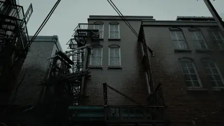 Resident Evil Requiem 2K Quad HD PC desktop wallpaper: moody desaturated alley of brick buildings with fire escapes, overhead wires and a gloomy sky.