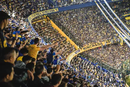 Panoramic 2K Quad HD desktop wallpaper of a packed Boca Juniors crowd in Argentina, fans in blue and yellow filling steep stands and waving banners.