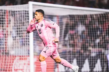 HD desktop wallpaper of an Inter Miami CF soccer forward in pink kit celebrating a goal by the net, sprinting with a finger to his lips amid a packed stadium.