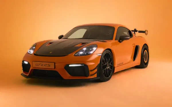 Orange Porsche 718 Cayman GT4 sports car, front three-quarter view in a studio with matching orange backdrop — 4K Ultra HD PC desktop wallpaper