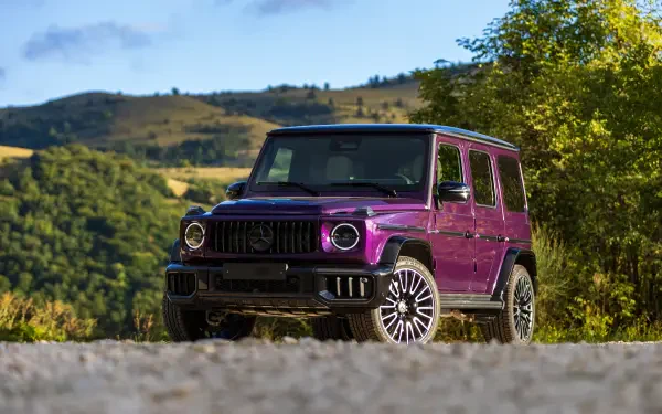 Purple Mercedes-AMG G63 SUV on a gravel road with green hills in the background — 5K Ultra HD PC desktop wallpaper and background.