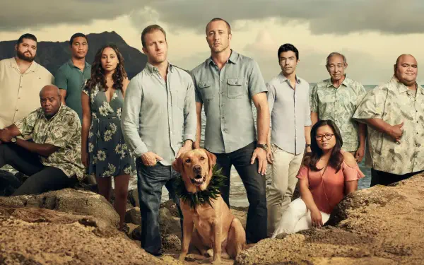 Hawaii Five-O 2K Quad HD PC desktop wallpaper shows a group on a rocky beach, two men at center with a dog, tropical hills and a cloudy sky behind.